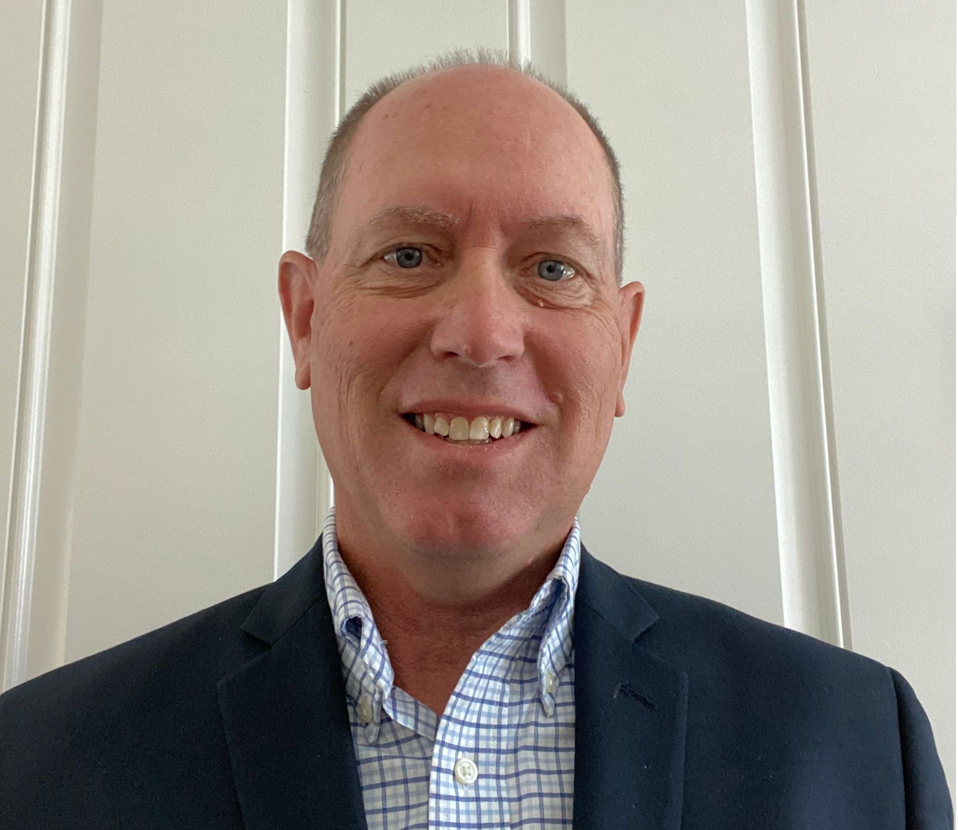 A man in a suit and plaid shirt is smiling for the camera.