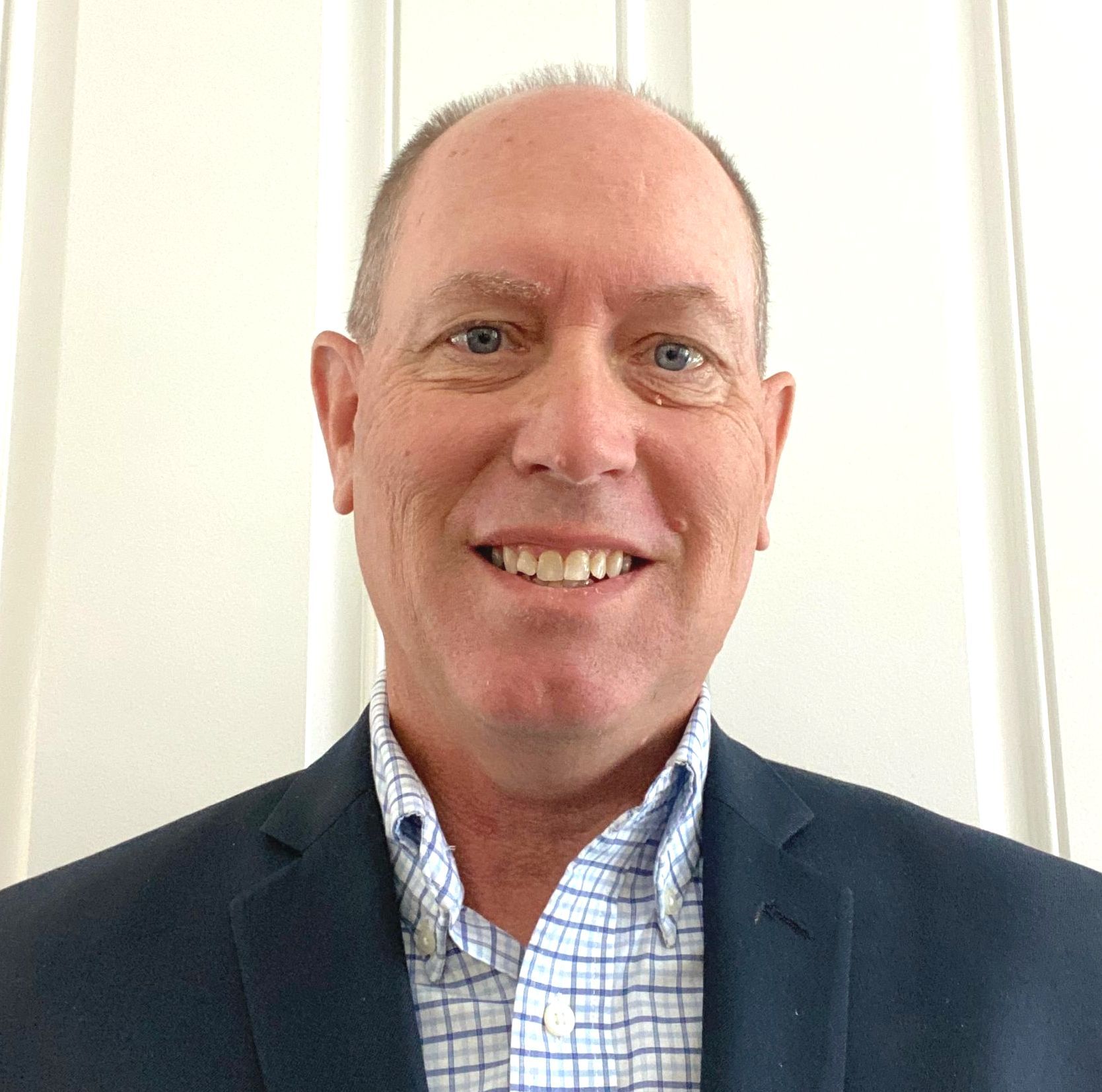 A man in a suit and plaid shirt is smiling for the camera.