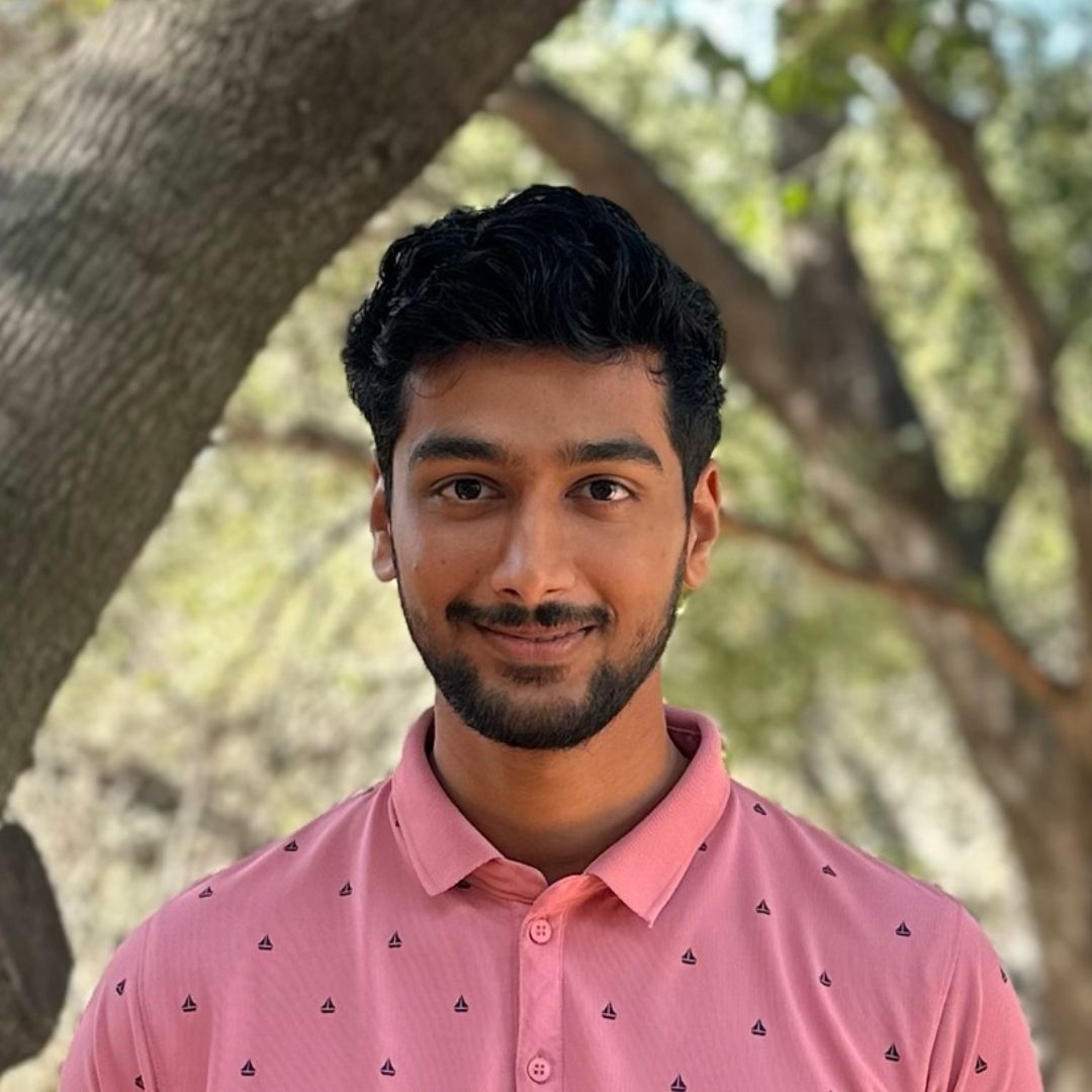 A young man with a beard is wearing a pink polo shirt.