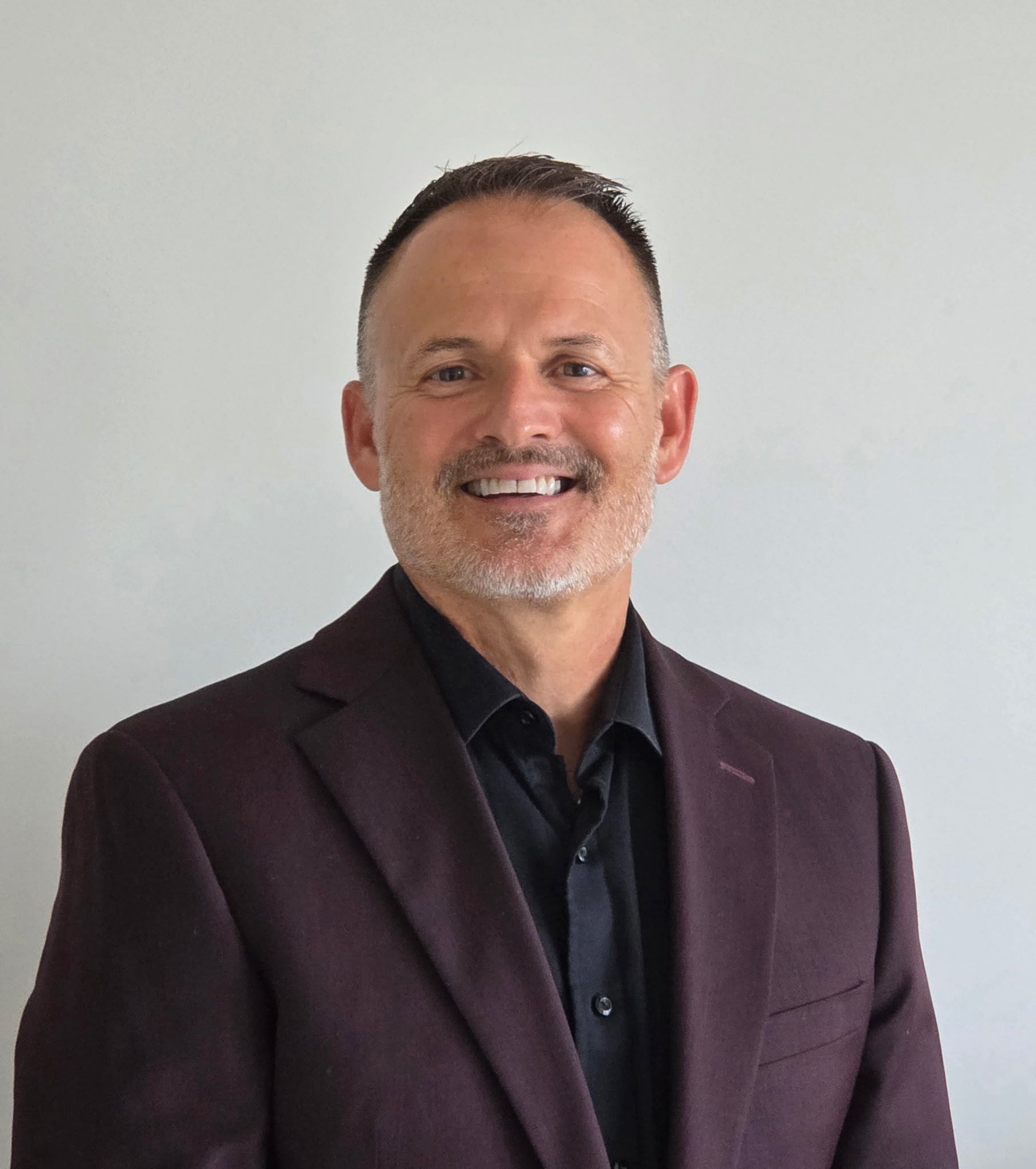A woman in a pink shirt and gray jacket is smiling in front of a tree.