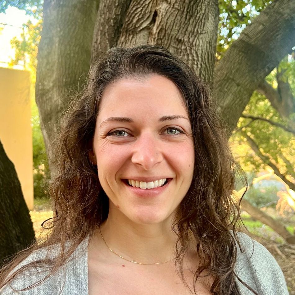 A woman in a striped shirt is smiling in front of trees.