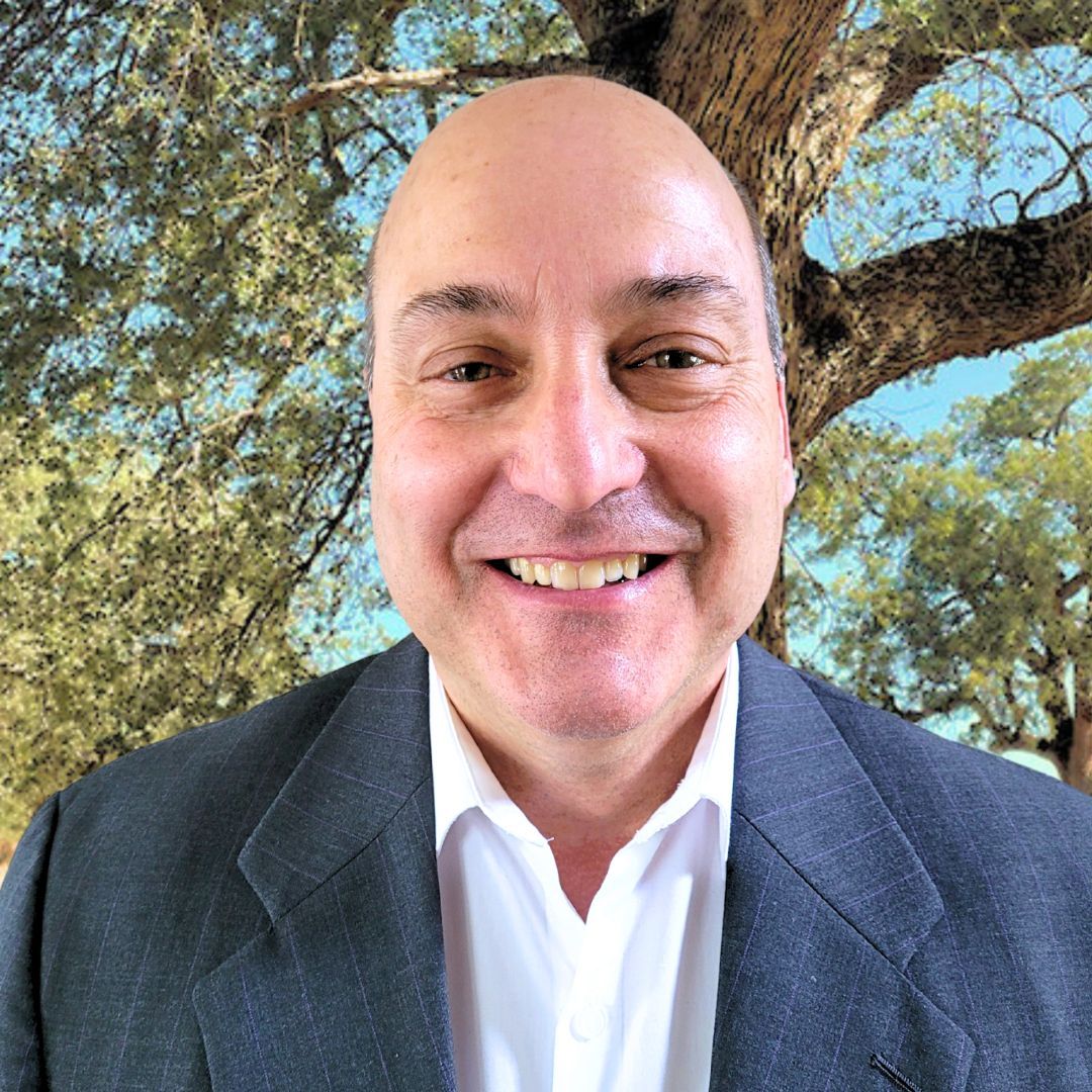 A man wearing glasses and a blue shirt smiles for the camera