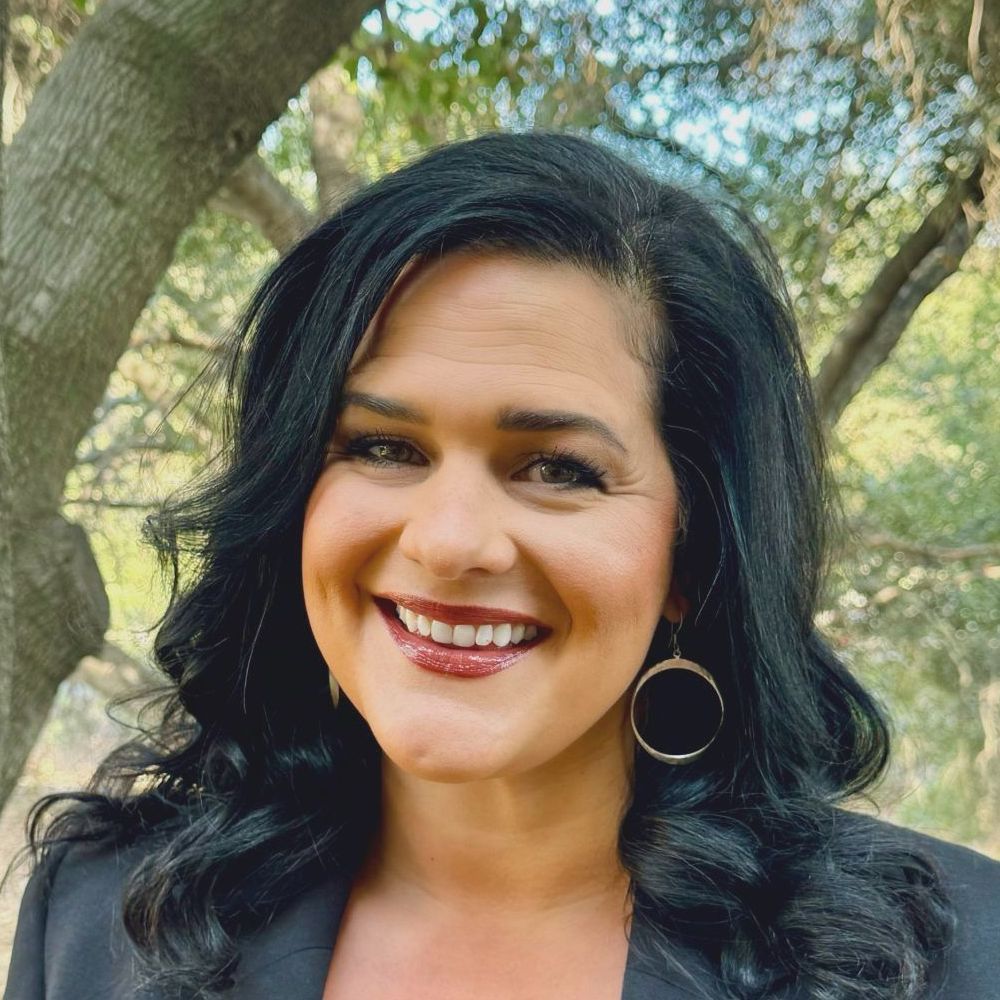 A woman wearing a black jacket and earrings is smiling for the camera.