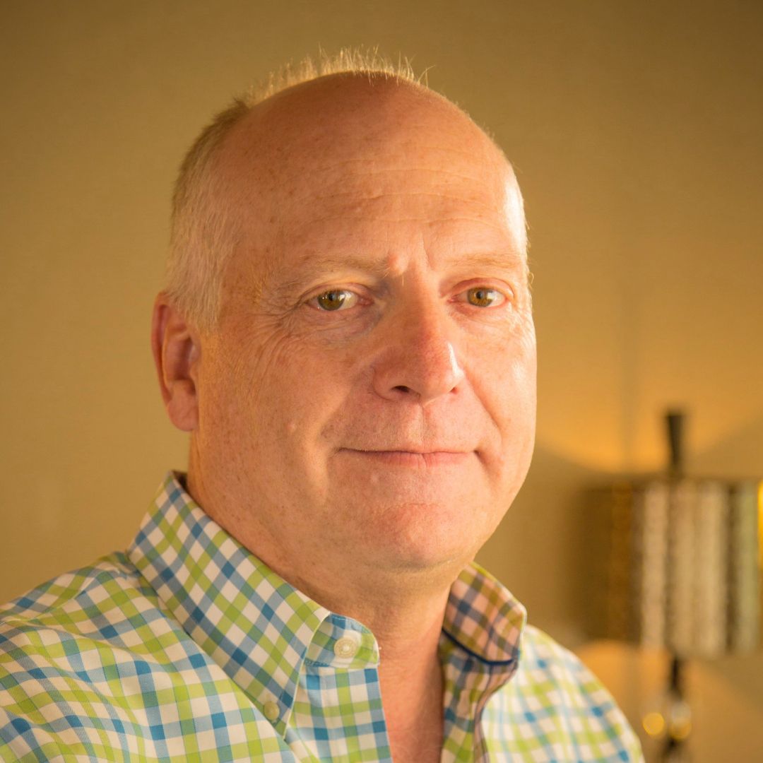 A bald man wearing a plaid shirt is smiling for the camera.