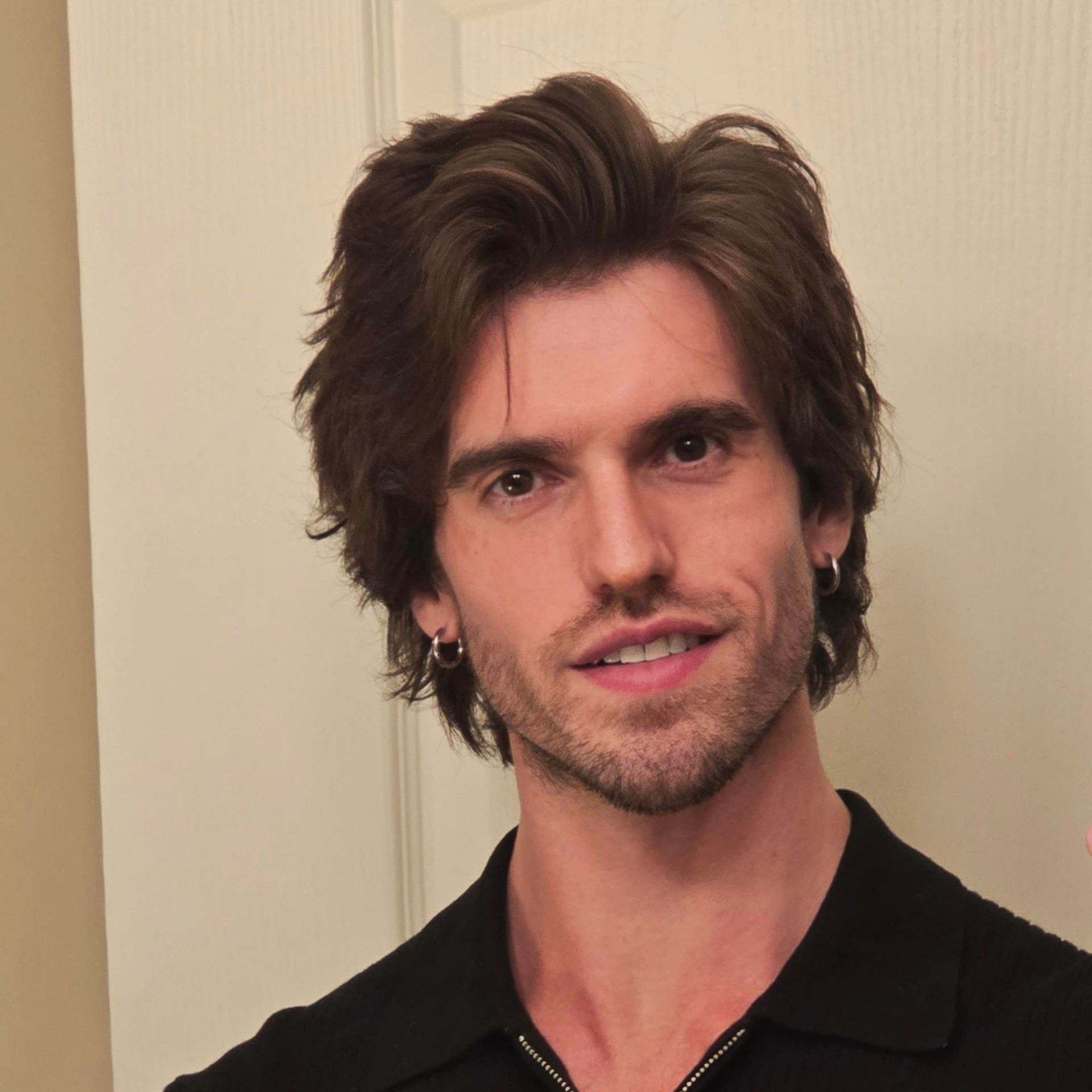 A woman in a pink shirt and gray jacket is smiling in front of a tree.