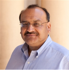 A man wearing glasses and a blue shirt smiles for the camera