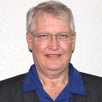 A man wearing glasses and a blue shirt is smiling for the camera.