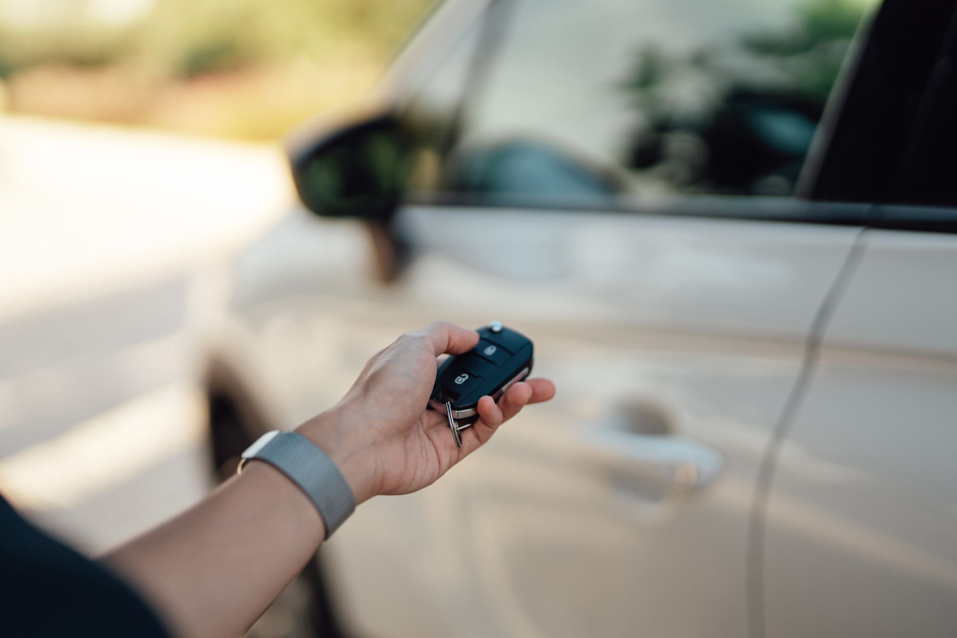Mano di una persona che tiene il portachiavi di un'auto, mentre apre la portiera bianca di un'auto, all'aperto alla luce del giorno.