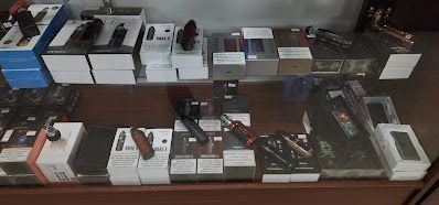Vaping products displayed on a glass shelf inside a store, containing various boxes and devices.