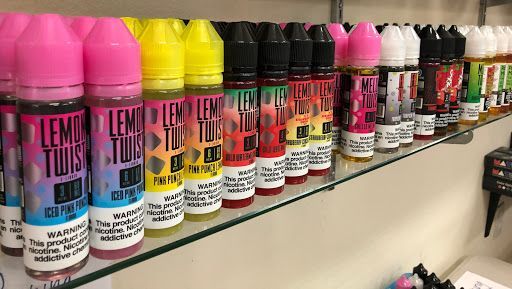 Shelf of colorful vape juice bottles, including Lemon Twist and other fruit flavors.