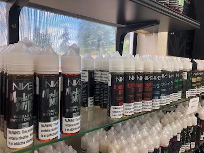 Bottles of vape liquid displayed on shelves in a store. Labels are black and white with various colors.