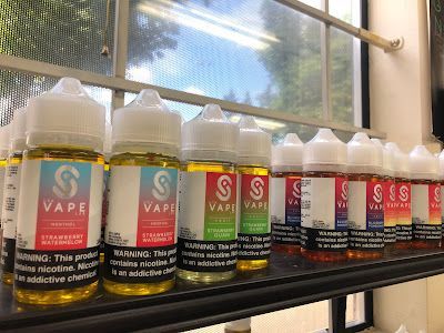 Bottles of vape liquid on a shelf; various flavors with colorful labels, set near a window.