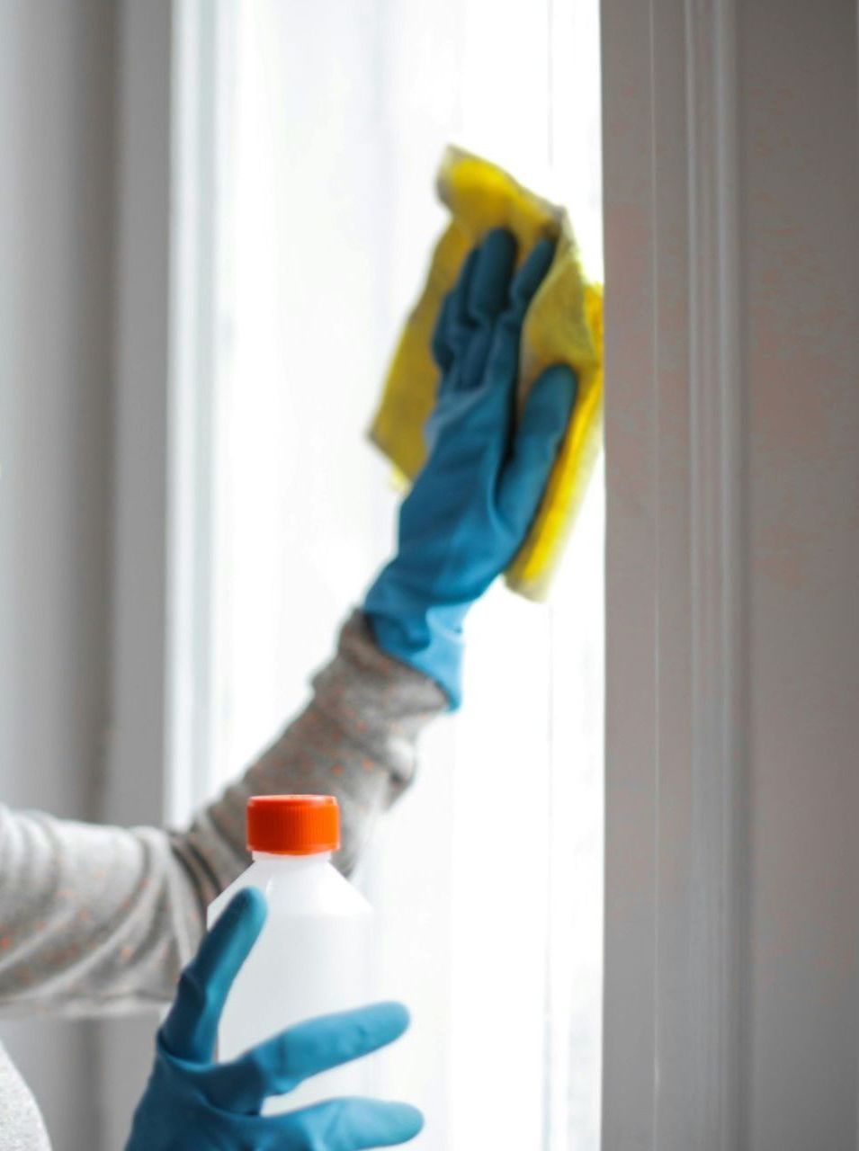 A person wearing blue gloves is cleaning a window with a yellow cloth.
