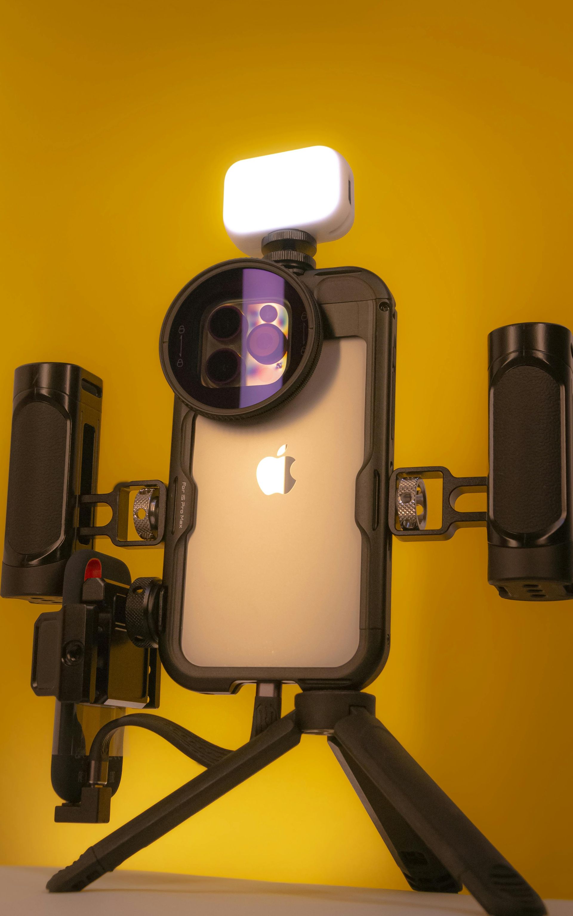 IPhone-Film-Setup auf Stativ, mit Weitwinkelobjektiv, Beleuchtung und externen Mikrofonen vor gelbem Hintergrund.