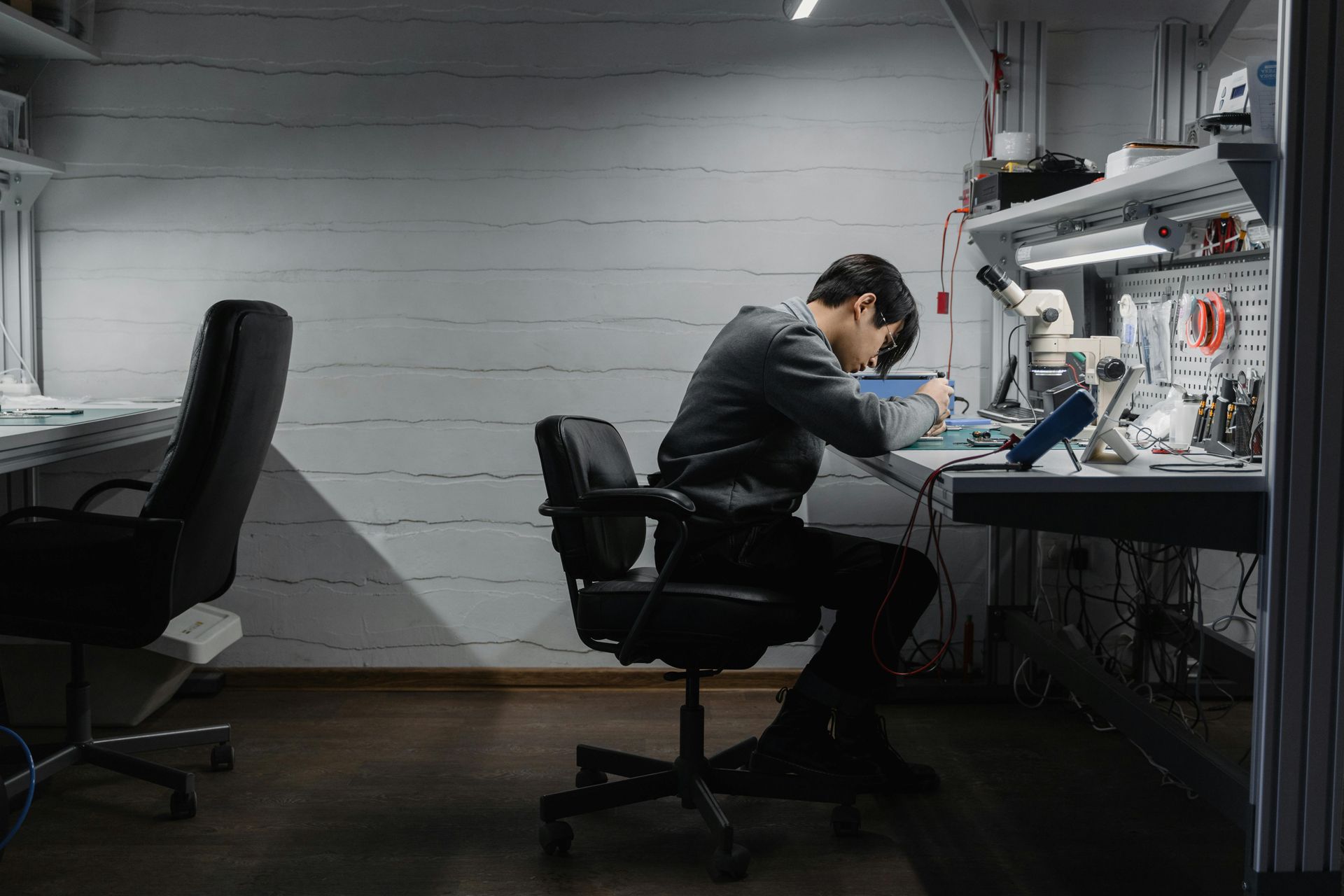 Eine Person arbeitet an einer Werkbank in einem schwach beleuchteten Raum an Elektronikgeräten.