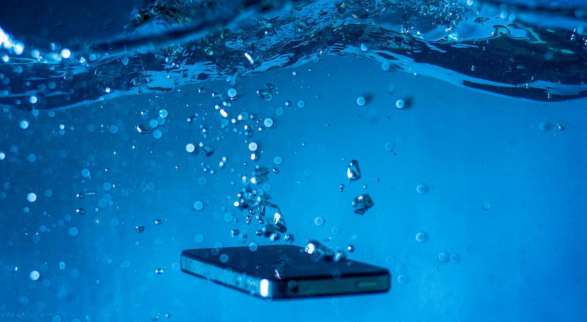 Smartphone in blauem Wasser, umgeben von Blasen.