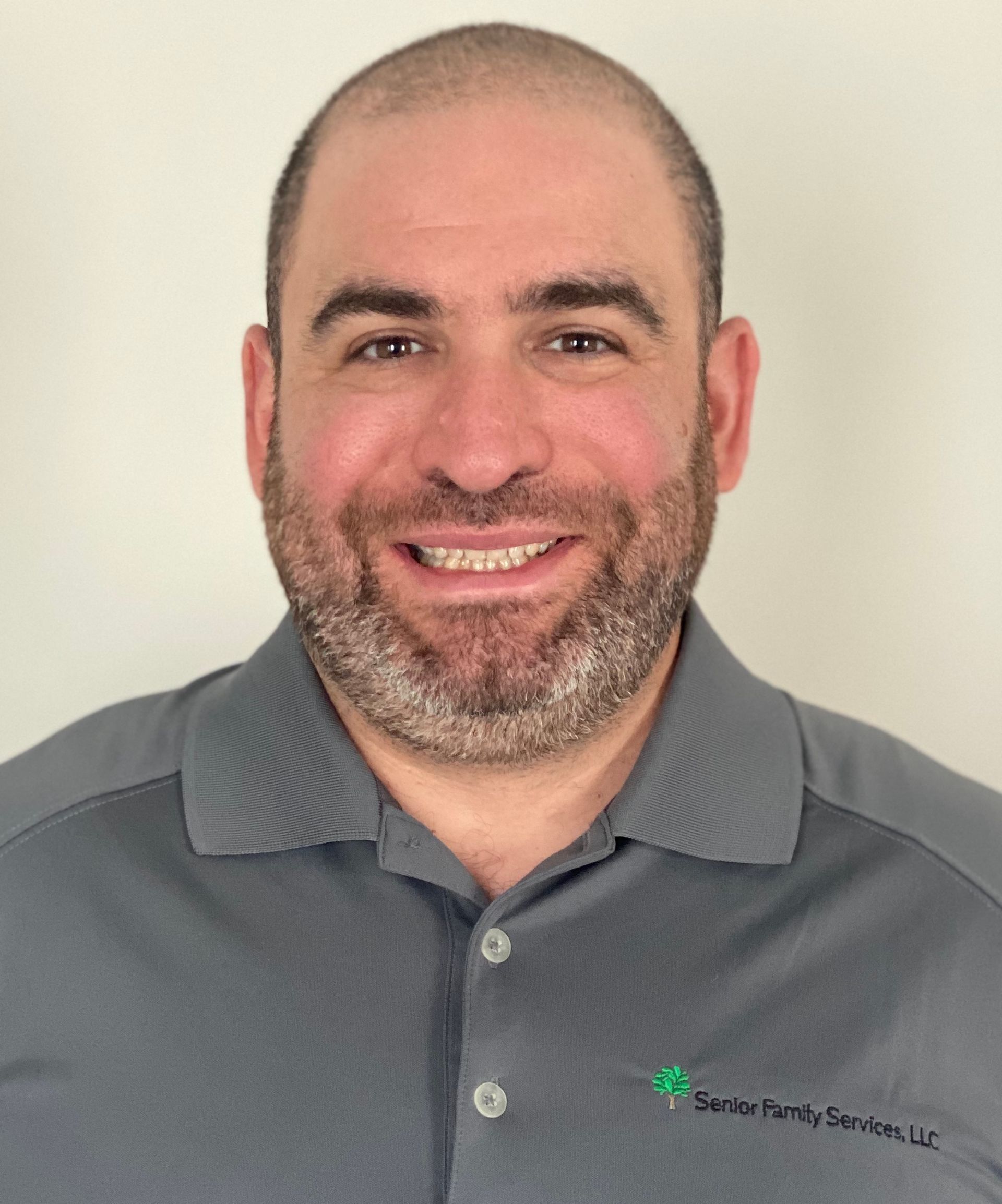 Man with short beard, smiling, wearing a grey polo shirt with a company logo.