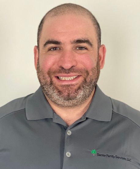 Man with short beard, smiling, wearing a grey polo shirt with a company logo.