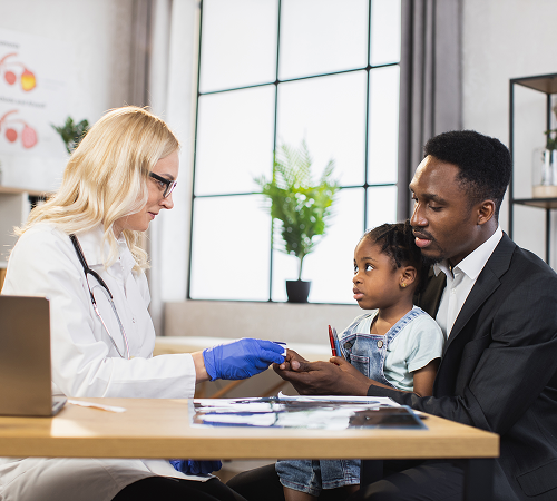Doctor examining a young girl's finger as her father watches in a doctor's office.