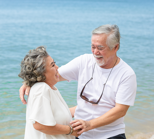 Elderly couple embracing and smiling on a beach, with ocean in background.
