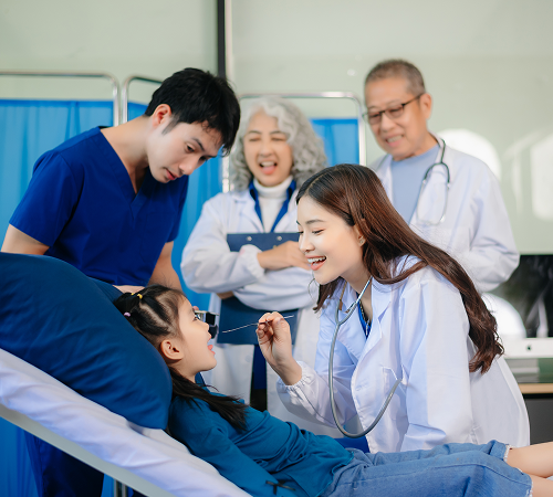 Doctors examining a girl in a hospital bed; others watch.