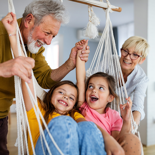 Grandparents and granddaughters playing on a swing, smiling.