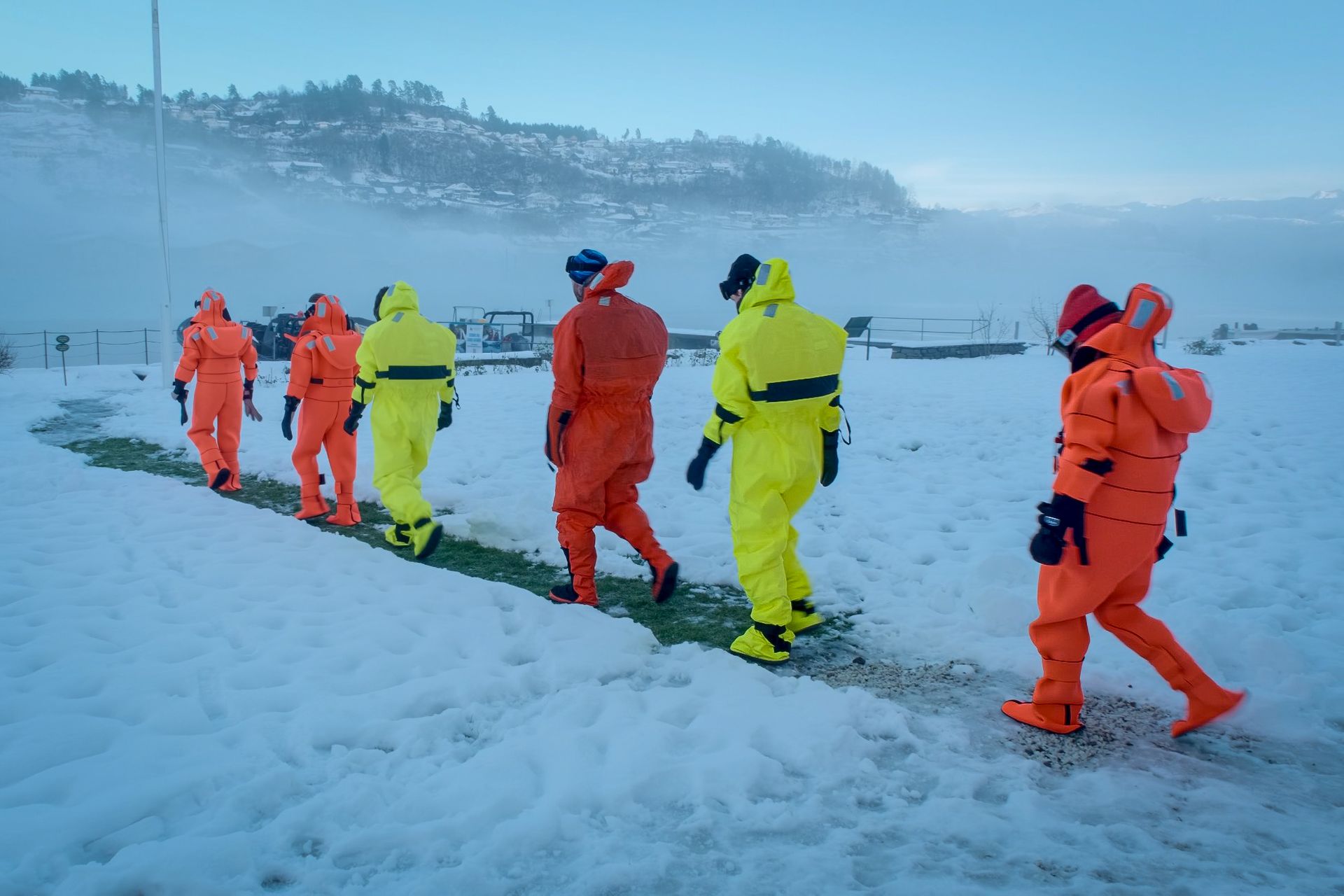 Woman sitting on rock, overlooking a fjord with mountains and snow.