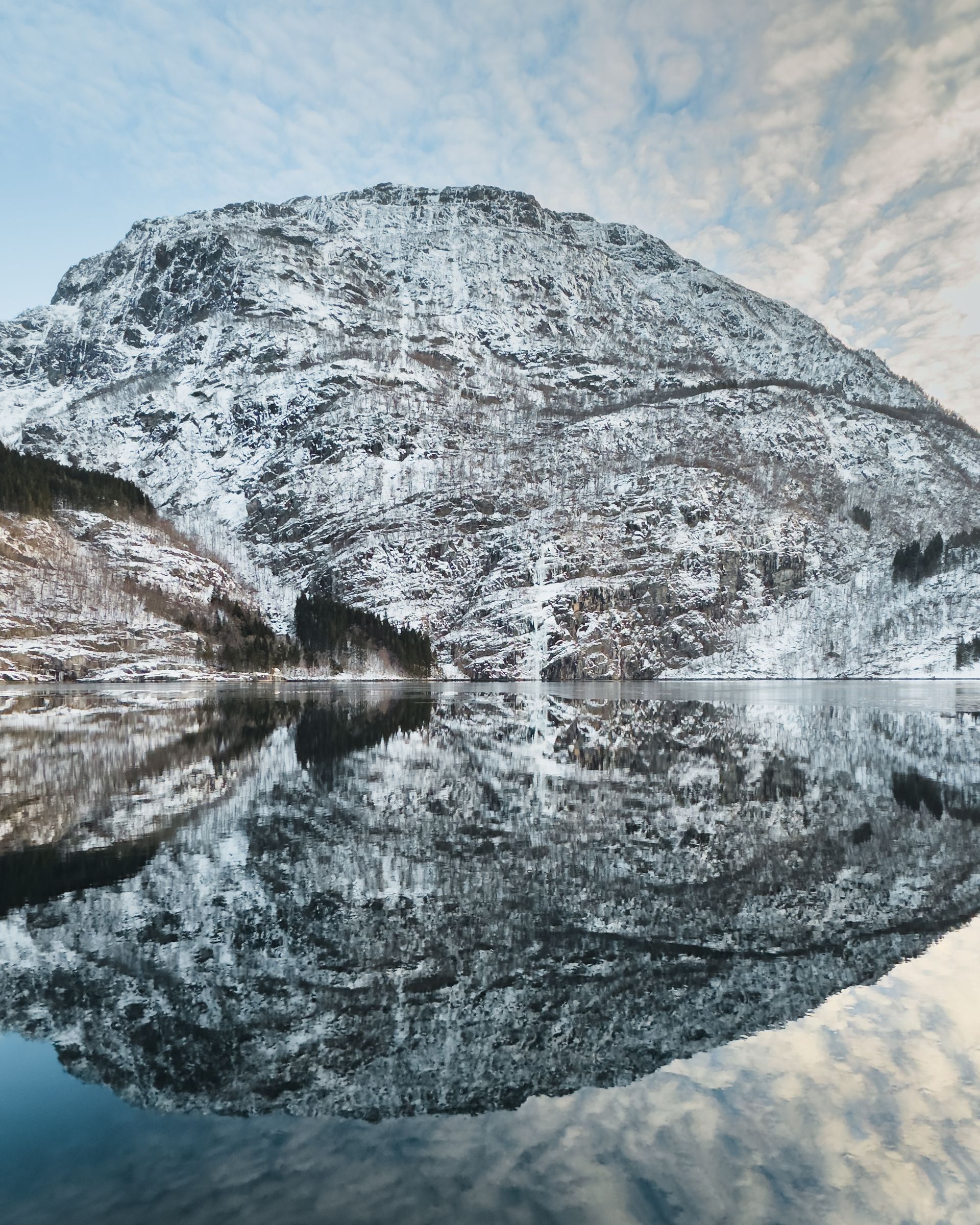Snowy mountain reflected in calm water. Cloudy sky.