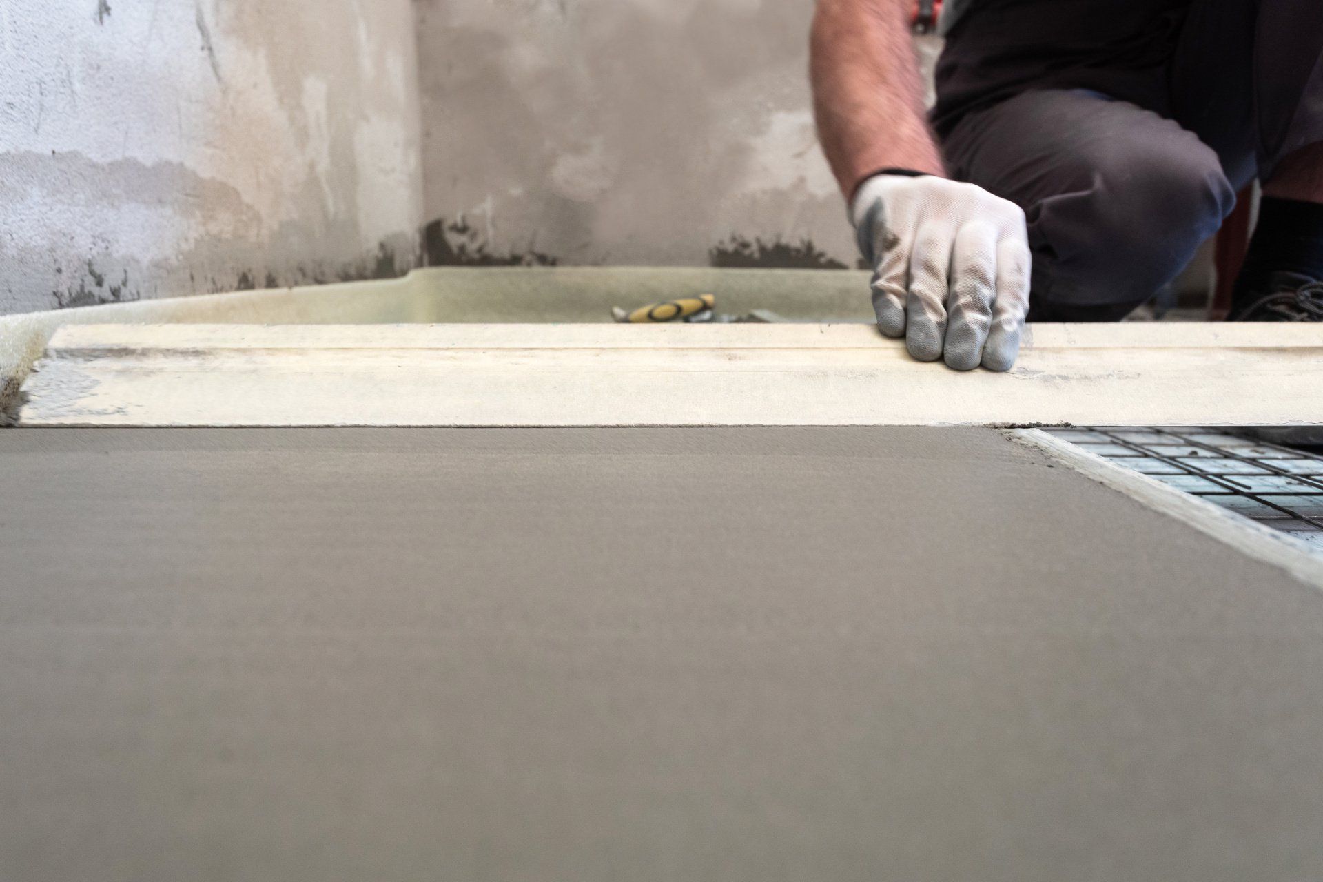 Construction worker using a level and screed to create a smooth indoor floor surface.