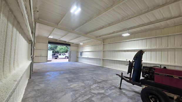 Interior of a large metal shed with concrete floor, open doorway, and farm equipment on the right.