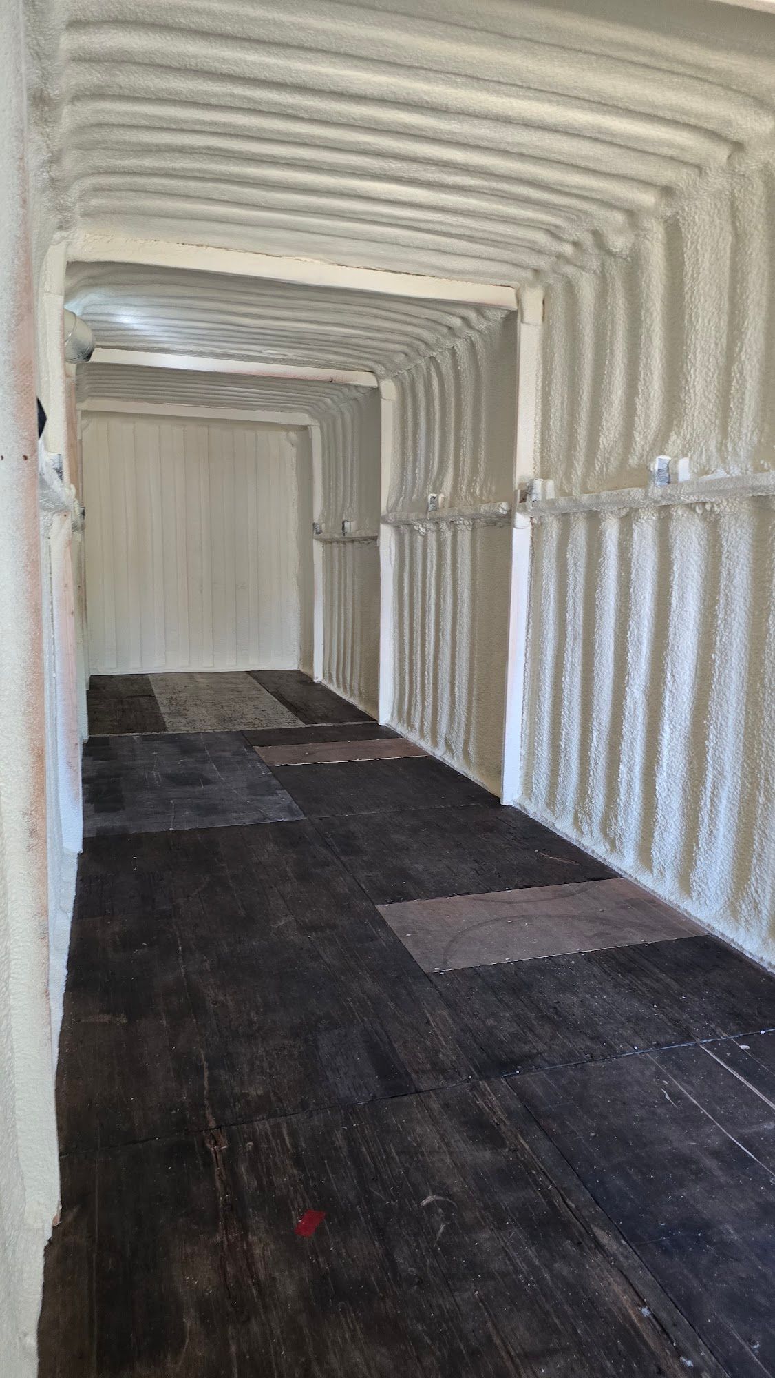 Curved white covered walkway with ribbed ceiling and dark floor leading to a closed door