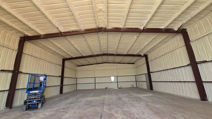 Empty warehouse interior with a blue scissor lift on the left and a large dirt mound in the center