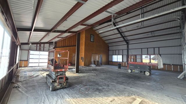 Interior of a metal workshop with a loft, open garage door, and two parked utility carts.