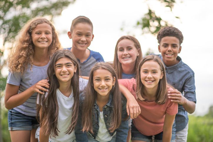 A group of 8th grader boys and girls smiling and leaning in toward the camera