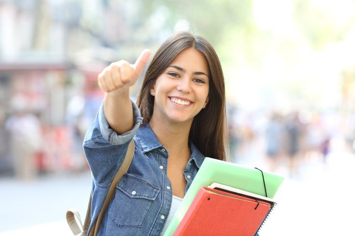 Student holding books smiling and giving a thumbs up.