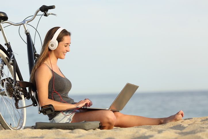 This is a photo of a girl leaning against a bike on a beach working on a laptop