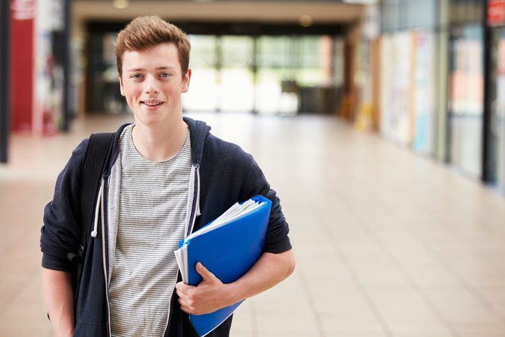 Teen boy walking in school hallway with notebook smiling