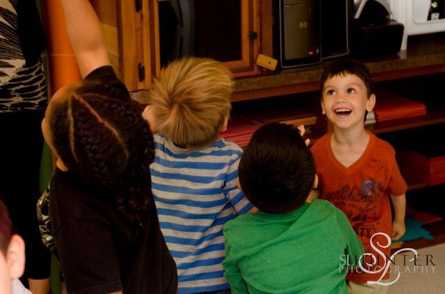 A Group of Children Are Sitting on The Floor Looking up At Something.