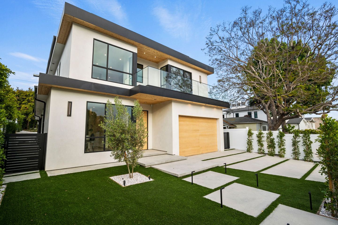 A large white house with a wooden garage door and a lush green lawn in front of it.