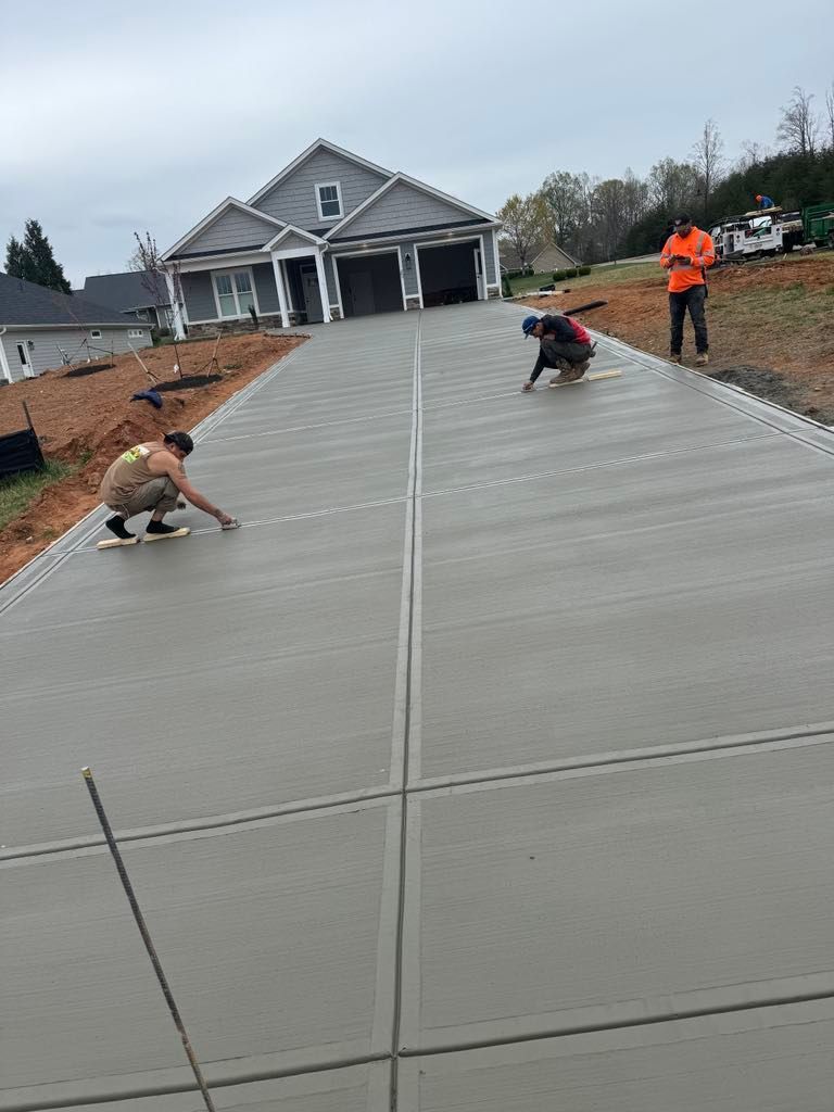 Two men are working on a concrete driveway in front of a house.