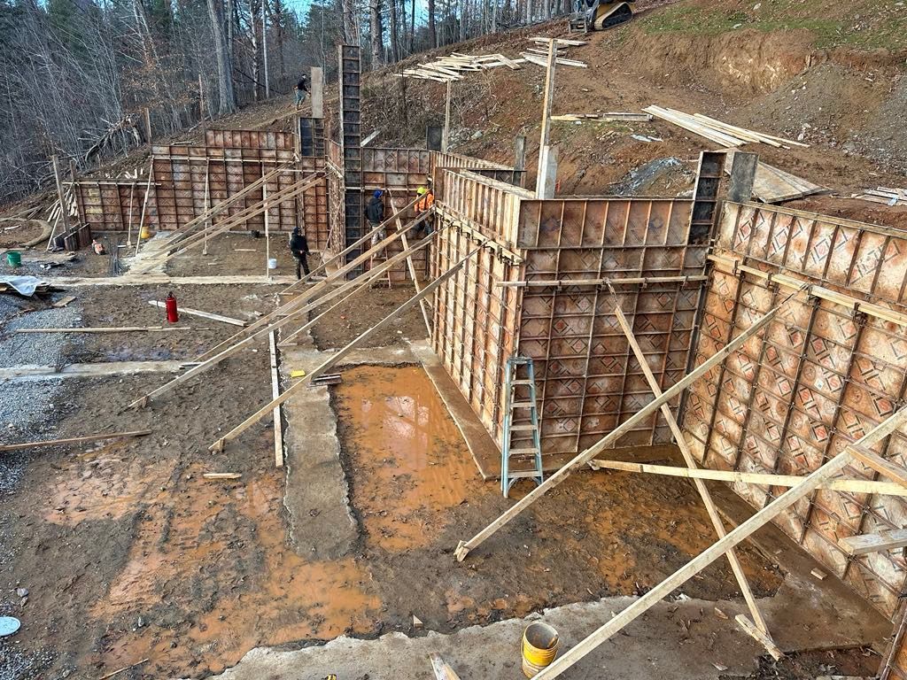 A large concrete wall is being built on top of a dirt hill.