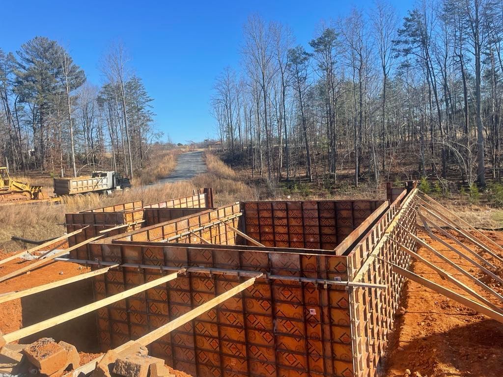 A large concrete wall is being built in a field with trees in the background.