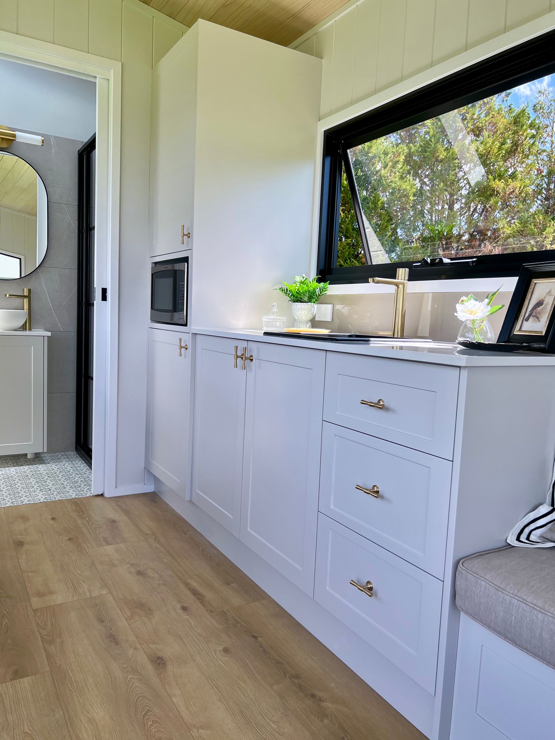A Kitchen With White Cabinets , Drawers , a Sink and a Window — Highlands Tiny Homes In Braemar, NSW
