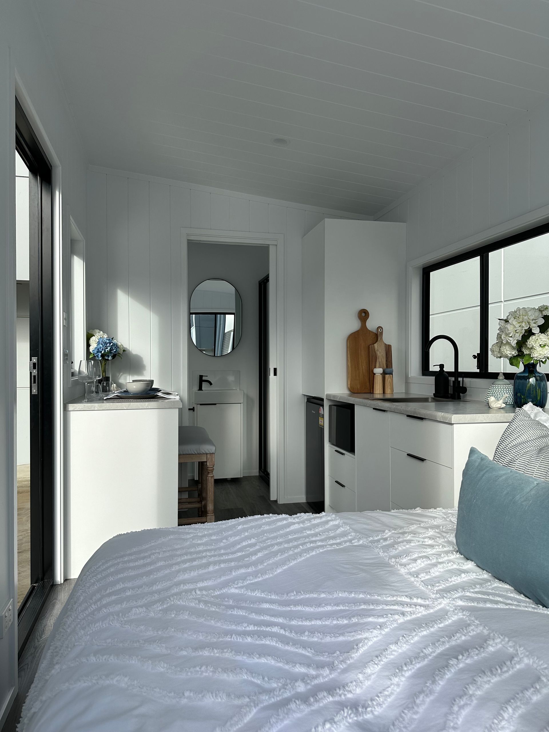 A Bedroom With a Bed and Pillows and a Kitchen in the Background — Highlands Tiny Homes In Braemar, NSW