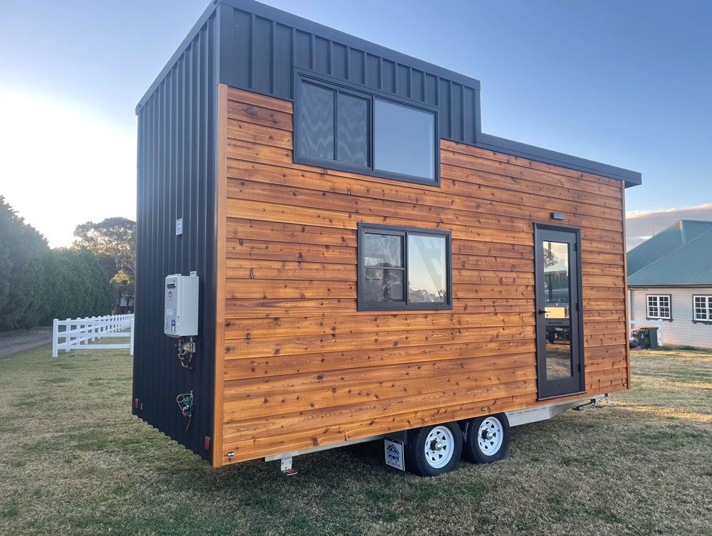 A Small Wooden House on Wheels is Parked in a Grassy Field — Highlands Tiny Homes In Braemar, NSW