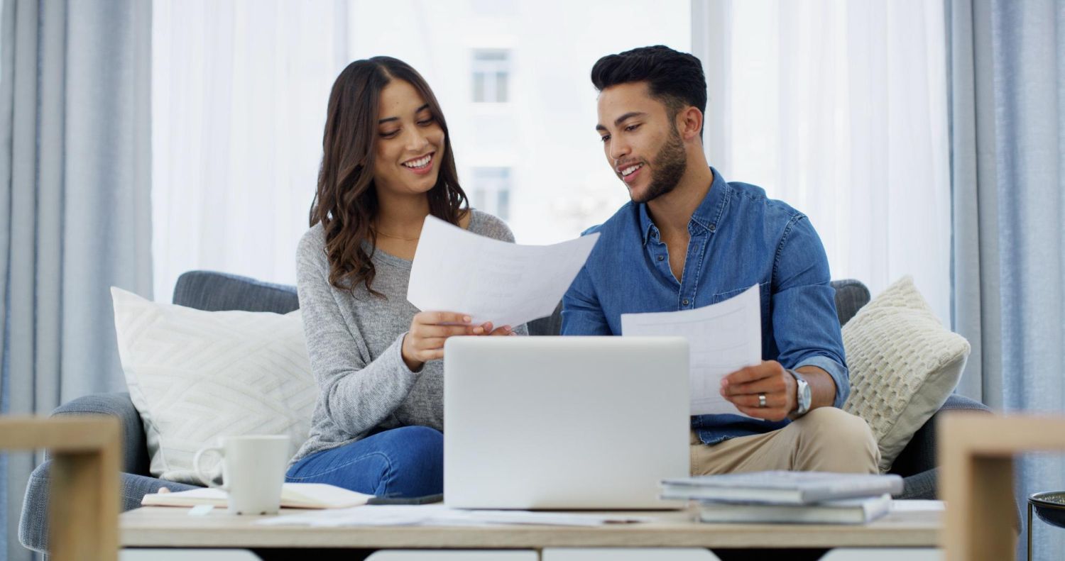 Couple looking at papers together with a laptop on a coffee table in a living room.