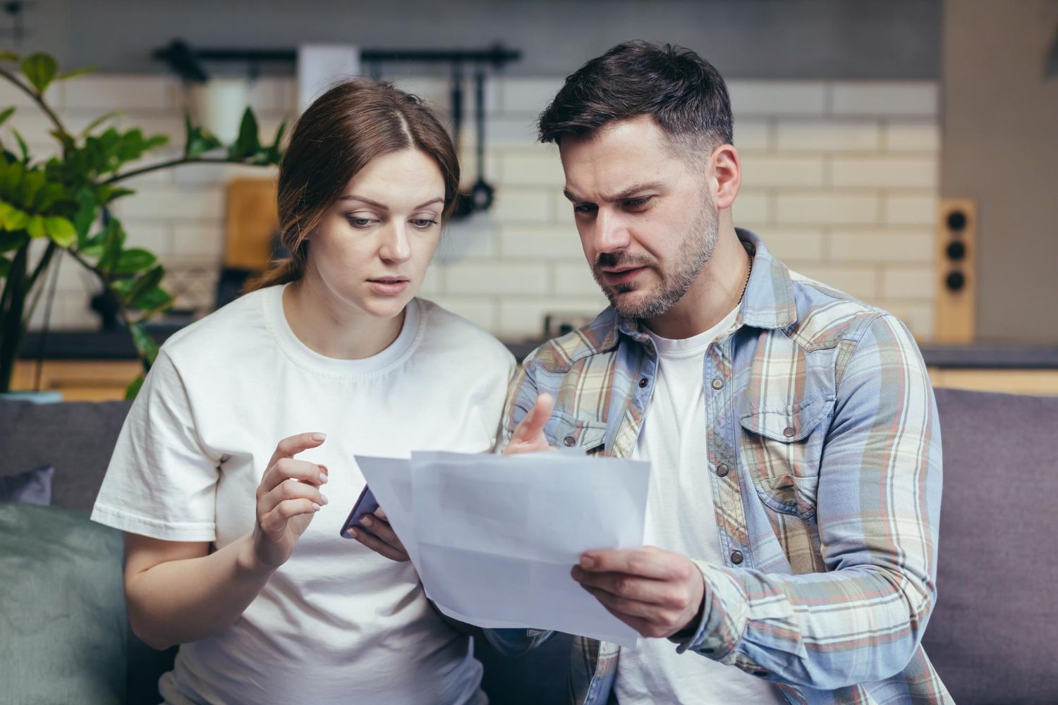 Couple looking at documents, appearing concerned, in a living room setting.