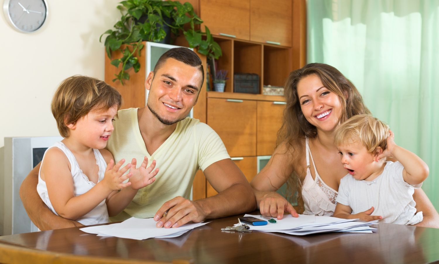 Family of four smiles together at a table, looking at papers.