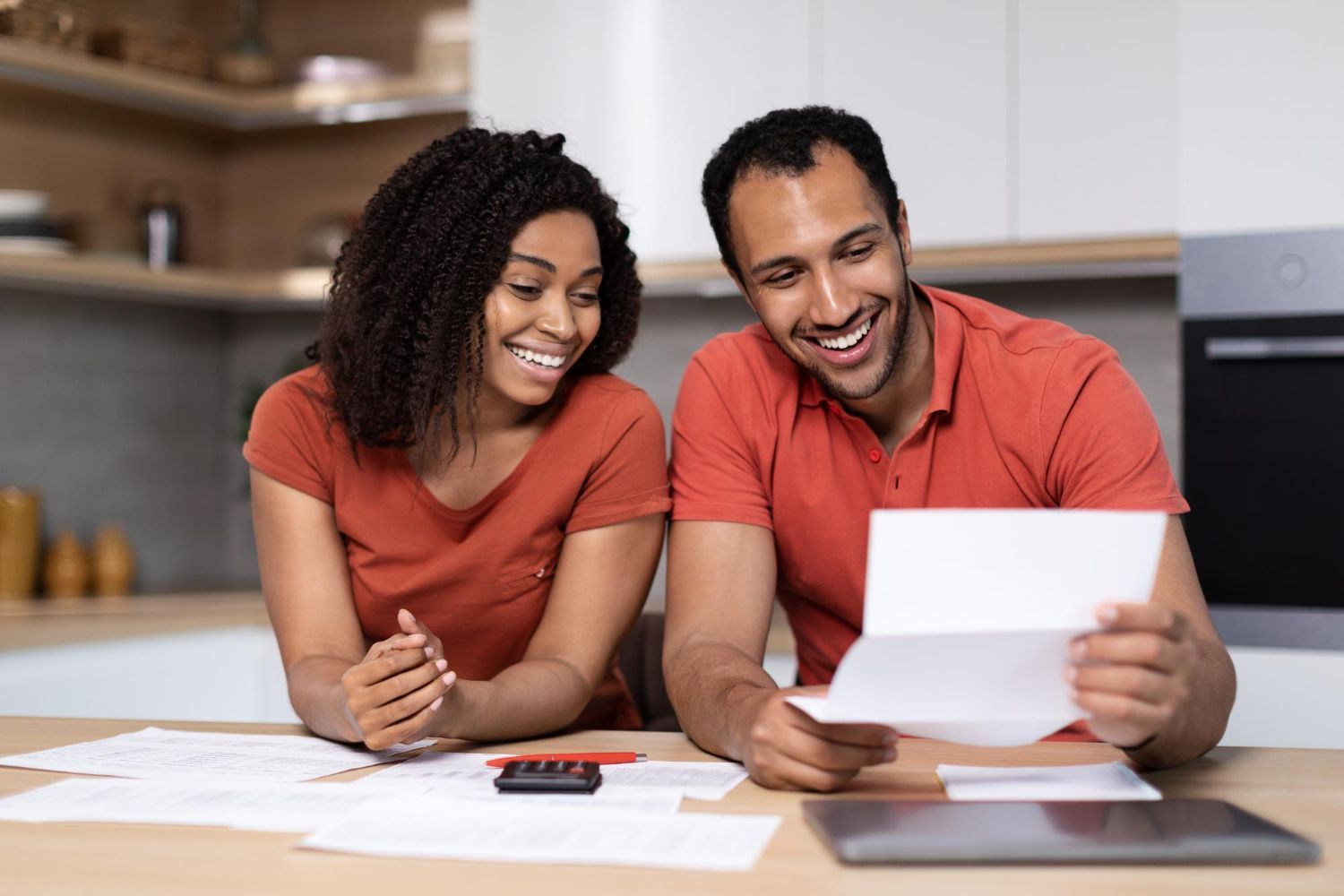 Couple smiling, reviewing paperwork at a kitchen table. They are looking at a document.