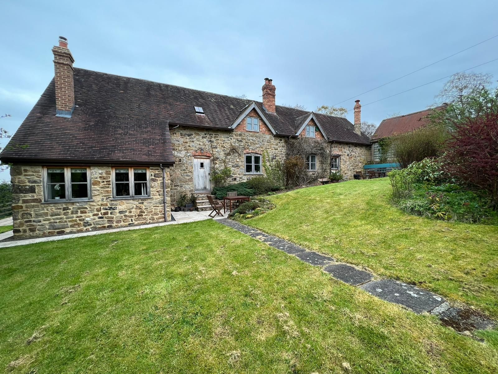 Stone cottage with green lawn and a pathway, cloudy sky overhead.